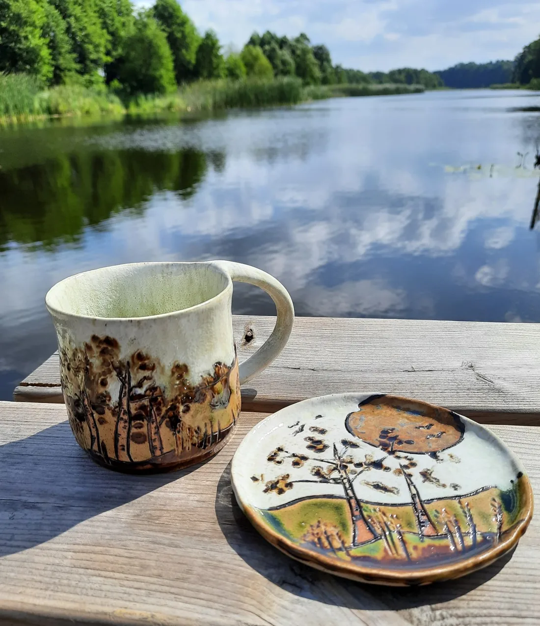 Ceramiczny kubek i talerz na pomoście nad jeziorem