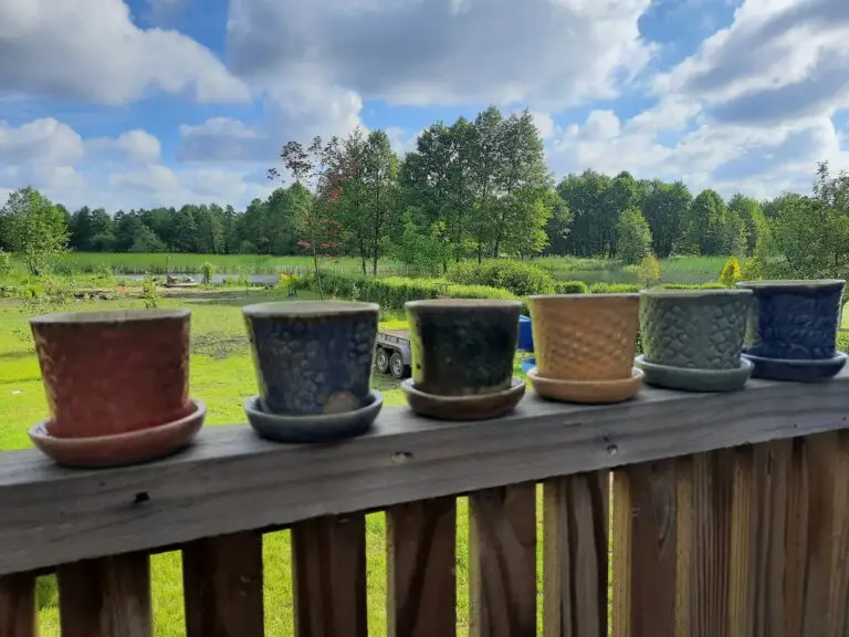 Kolorowe ceramiczne doniczki na drewnianej balustradzie, w tle ogród