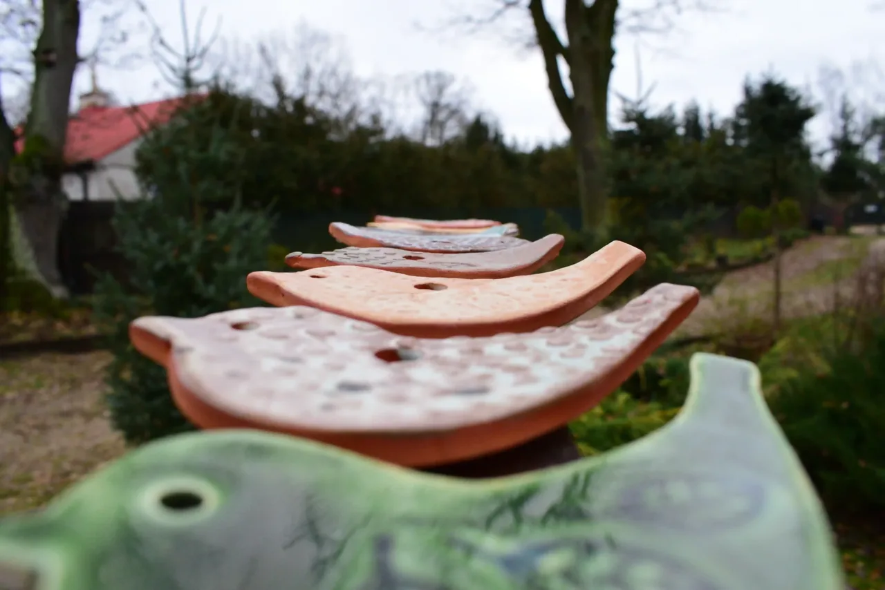 Płaskie ceramiczne formy z otworami na zielonym stole, w tle ogród