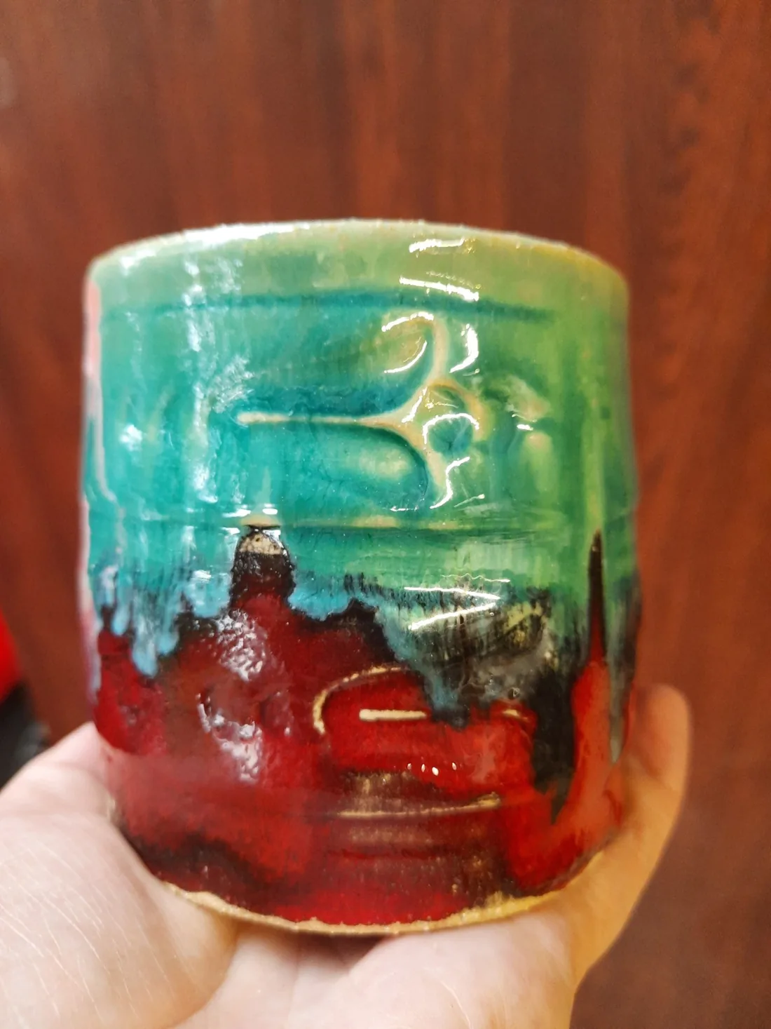 Wielobarwny szkliwiony kubek ceramiczny prezentowany w dłoni